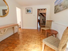 A hallway with wooden floor a console table a round wall mirror two woven chairs and a small wooden table at Orme Villa in Llandudno