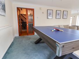 A room with a ping pong table, paddles and ball with a sofa and framed pictures on the wall at Orme Villa in Llandudno