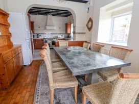 A dining area with a metal table and woven chairs next to a kitchen with wooden cabinets and a white refrigerator at Orme Villa in Llandudno