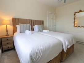 A bedroom with two single beds joined together with white bedding a bedside table with a lamp a door and a decorative mirror on the wall at Orme Villa in Llandudno