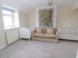 A room with a beige sofa between two white baby cribs and a window with a radiator below at Orme Villa in Llandudno