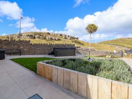 An outdoor patio area with a wooden planter containing plants and a small tree a stone wall a grassy area and a hot tub at Orme Villa in Llandudno