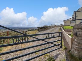 A gravel driveway with a metal gate labeled Orme Villa next to a house and overlooking a landscape with hills and clouds at Orme Villa in Llandudno