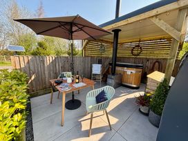 An outdoor patio area with a wooden table, two chairs, a large umbrella, a hot tub under a wooden pergola, and potted plants at Oh Deer in Ashbourne
