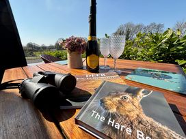 A wooden table outside with binoculars books glasses a bottle of prosecco and a flower pot at Oh Deer in Ashbourne