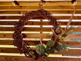 A decorative wreath made of twigs with green leaves and an antler hanging on a wooden slatted wall