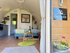 An interior view of a small curved cabin showing a bed with green blanket a small wooden table with a bottle and flowers kitchen area and a door leading to a bathroom at Oh Deer Ashbourne