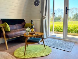 A sitting area with a leather loveseat green pillows a small wooden table with a bottle flowers and a book next to glass doors and rugs at Oh Deer in Ashbourne