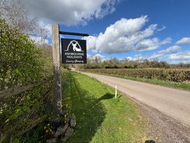 A wooden post with a hanging sign for Ashbourne Holidays luxury glamping next to a road and hedges in Ashbourne
