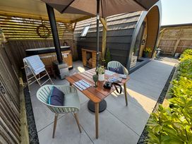 An outdoor patio with a wooden table and two chairs under an umbrella next to a small cabin and hot tub at No Deer in Ashbourne