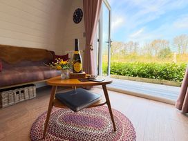 A living area with a wooden coffee table holding a bottle and a small vase of flowers next to a brown sofa and an open door showing greenery outside at No Deer in Ashbourne