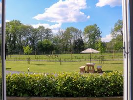 A garden with a wooden table and benches under an umbrella overlooking grassy fields and trees at No Deer in Ashbourne
