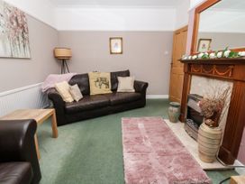 A living room with a brown leather sofa and armchair a wooden coffee table a fireplace and a pink rug at The Hollies in Prestatyn