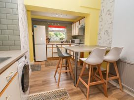 A kitchen with a high table and three chairs a refrigerator washing machine and cabinets at The Hollies in Prestatyn