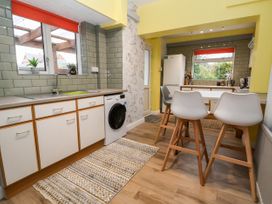 A kitchen with white cabinets a washing machine a dining table with white chairs and windows with red blinds at The Hollies in Prestatyn