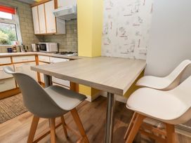 A kitchen area with a wooden table and three chairs next to kitchen cabinets and appliances at The Hollies in Prestatyn