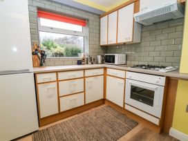 A kitchen with white cabinets a white fridge a white oven a gas stove a microwave a kettle and a window with a red blind at The Hollies in Prestatyn