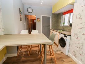 A kitchen with a wooden table and chairs a washing machine under counter and a window with plants at The Hollies in Prestatyn