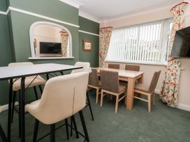 A dining area with two tables and chairs near a window with vertical blinds and floral curtains at The Hollies in Prestatyn