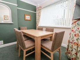 A dining room with a wooden table and six upholstered chairs next to a window with vertical blinds and floral curtains at The Hollies in Prestatyn