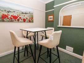 A dining area with a white square table and four beige high chairs with a green and cream wall at The Hollies in Prestatyn