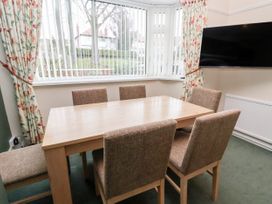 A dining room with a wooden table six chairs floral curtains and a wall-mounted television at The Hollies in Prestatyn