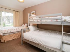 A bedroom with a bunk bed and a single bed with rainbow bedding near a window at The Hollies in Prestatyn