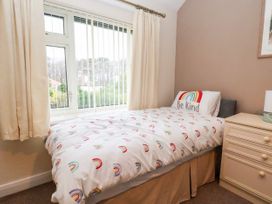A bedroom with a single bed with rainbow bedding and a bedside table with a lamp at The Hollies in Prestatyn