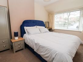 A bedroom with a double bed a bedside table with a lamp a wardrobe and a window with vertical blinds at The Hollies in Prestatyn