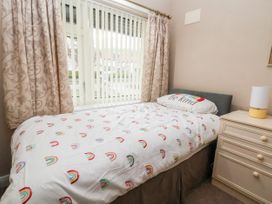 A single bed with rainbow patterned bedding and a be kind pillow next to a bedside table with a lamp
