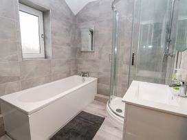 A bathroom with a bathtub a glass shower enclosure a sink and a window at The Hollies in Prestatyn
