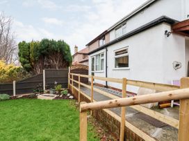 A backyard with a green lawn and wooden railing next to a white house exterior at The Hollies in Prestatyn