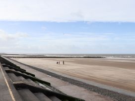 A beach with three people walking on the sand near a concrete promenade and the sea at The Hollies in Prestatyn