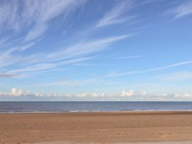 A sandy beach with calm sea and wind turbines on the horizon under a blue sky with clouds at The Hollies in Prestatyn