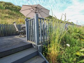 An outdoor deck with a table and chairs under an umbrella at 7 Beachdown in Challaborough