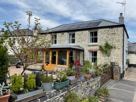 A stone house with solar panels on the roof and potted plants in front at Woodbine Cottage in Mylor Bridge Nr Falmouth