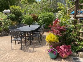 A patio with a black metal table and chairs surrounded by plants and flowers at Woodbine Cottage in Mylor Bridge Nr Falmouth