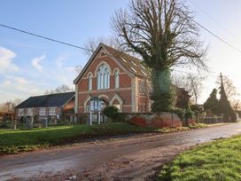 A building with a signboard and trees near a gravel road at The Stables at Hall Barn near Wattisfield near Walsham-Le-Willows