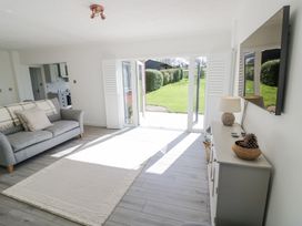 A living room with a gray sofa a white rug a cabinet with a lamp and bowl and double glass doors leading to a garden at New House Farm in Wappenbury near Leamington Spa
