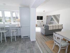 A kitchen with two chairs by a window and an adjacent living room with a sofa and a wall-mounted TV at New House Farm in Wappenbury near Leamington Spa