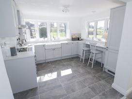 A kitchen with white cabinets two chairs and large windows overlooking a green field at New House Farm in Wappenbury near Leamington Spa