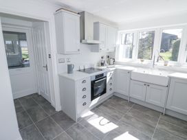 A kitchen with gray cabinets white countertops an oven a sink under windows and a door leading to a laundry room at New House Farm in Wappenbury near Leamington Spa