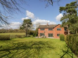 A red brick house with a tiled roof a garden table and chairs a grassy lawn and trees at New House Farm in Wappenbury near Leamington Spa