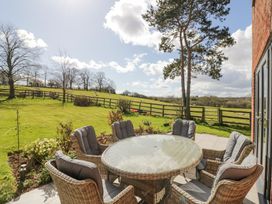 An outdoor patio with a round glass table and six cushioned wicker chairs looking out to a fenced grassy field with trees at New House Farm in Wappenbury near Leamington Spa