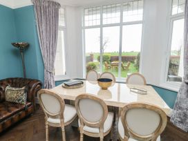 A dining area with six chairs around a marble table next to large windows showing a garden outside at Russell House in Paignton