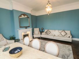 A living room with a white sofa and armchairs a mirror above the fireplace and a dining table with chairs at Russell House in Paignton