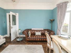 A room with a brown leather sofa blue walls a white door a glass side table and a marble table with chairs Russell House Paignton