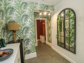 A hallway with green leaf wallpaper a lamp on a cabinet and a decorative wall mirror with greenery at Russell House Paignton