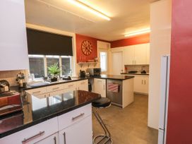 A kitchen with black countertops white cabinets a stool and a window with a black blind at Russell House Paignton