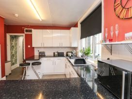 A kitchen with white cabinets black countertops bar stools a microwave and a window with a black blind at Russell House in Paignton